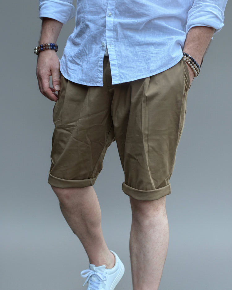 Person wearing a white shirt, brown shorts, and white sneakers in front of light grey backdrop.
