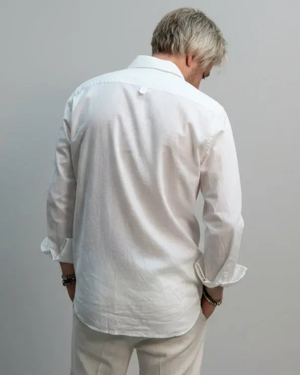 Model wearing a white shirt and white pants in front of light grey backdrop