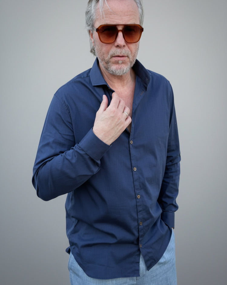 Person wearing a navy blue button-up shirt in front of light grey backdop