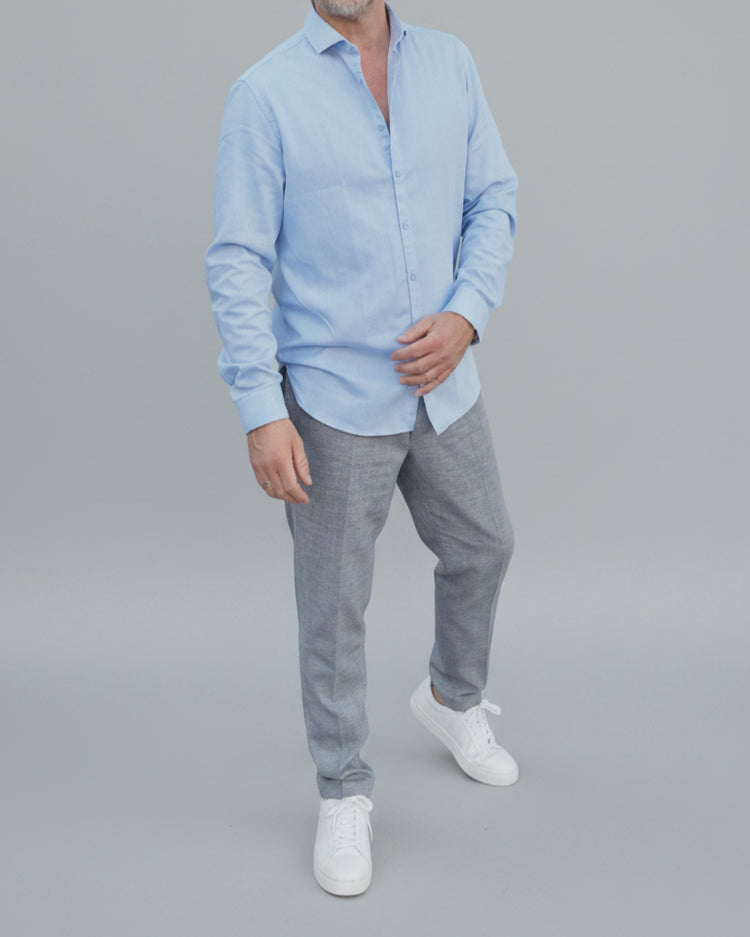Man in light blue shirt and gray pants standing in front of light grey backdrop