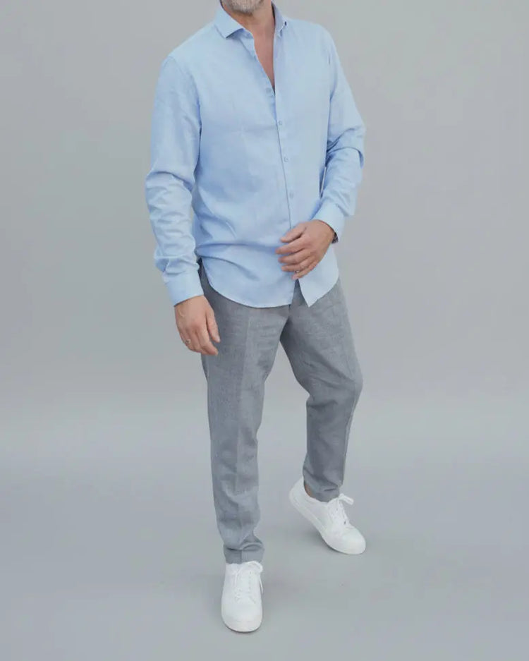Man in light blue shirt and gray pants standing in front of light grey backdrop