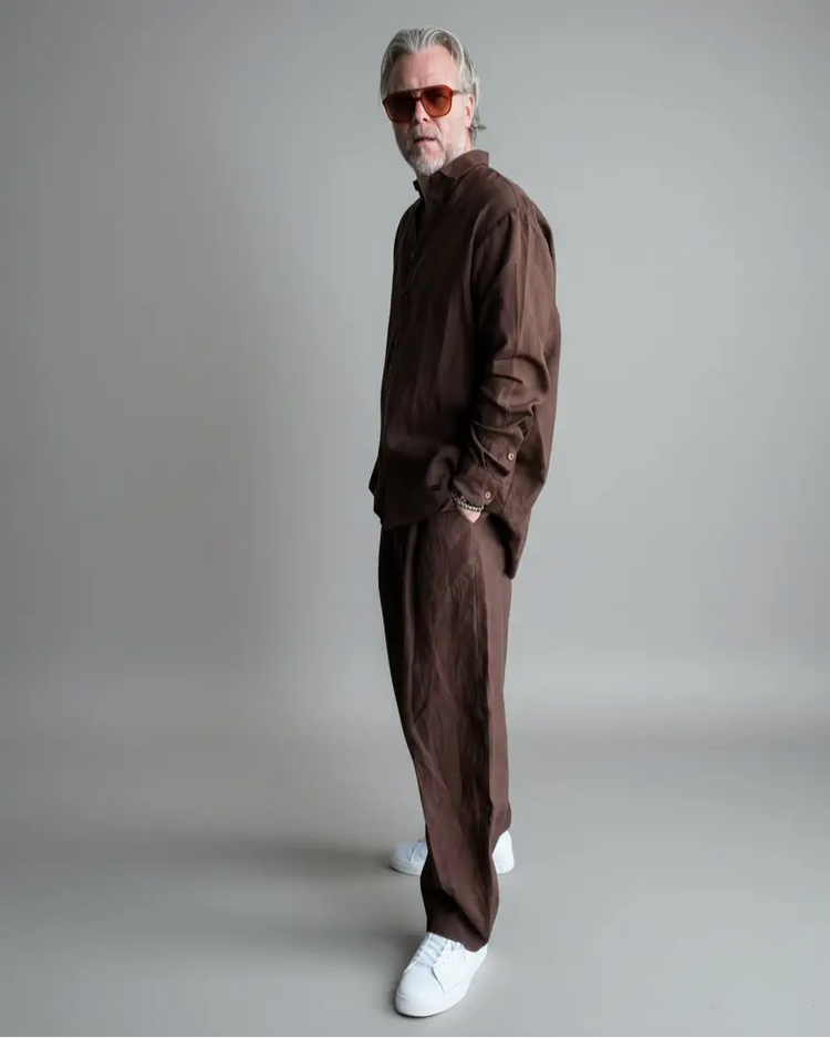 Man in a brown outfit standing against light grey backdrop