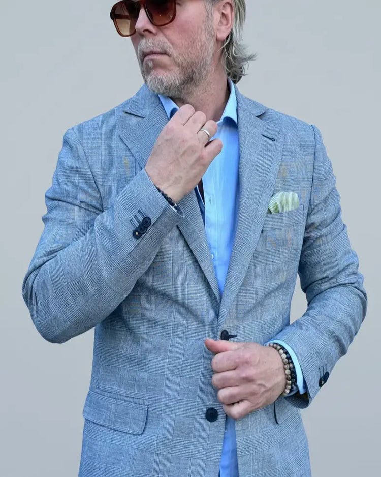 Man in a gray, blue checked suit standing in front of a light grey backdrop.