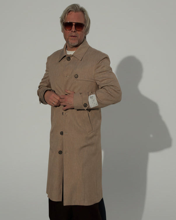 MODEL WEARING A BEIGE COAT IN FRONT OF A GREY BACKDROP