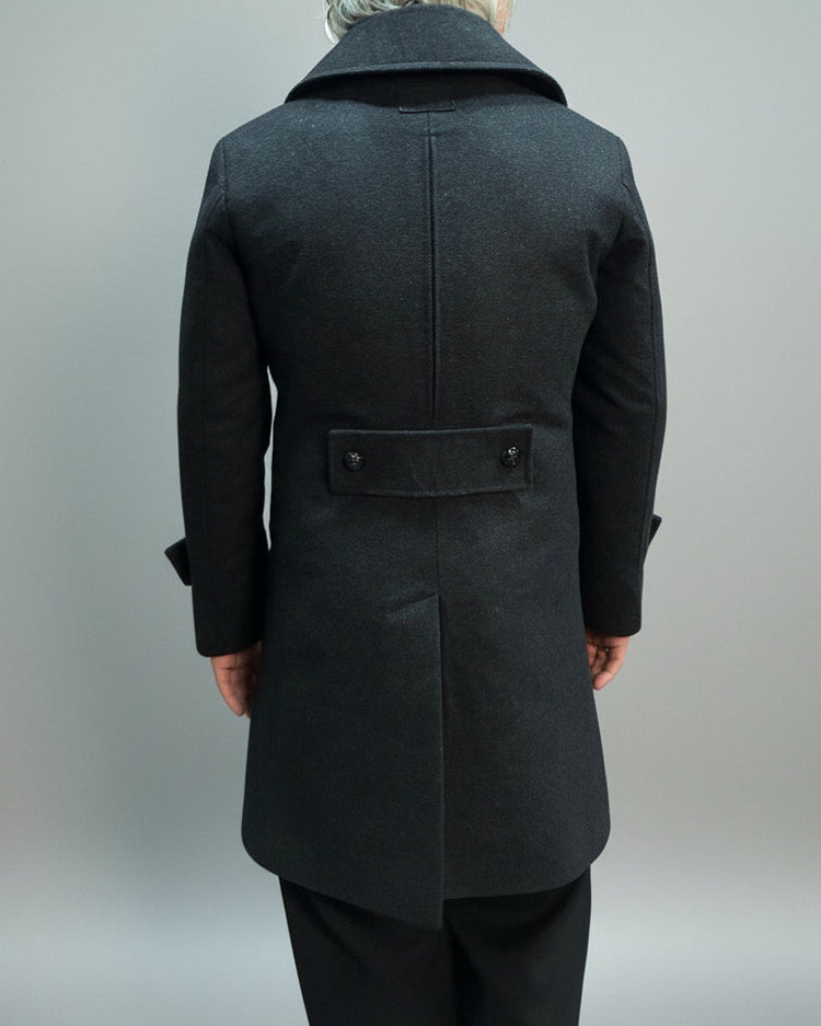 Person wearing a Grey coat standing on a beige mat with a blurred background