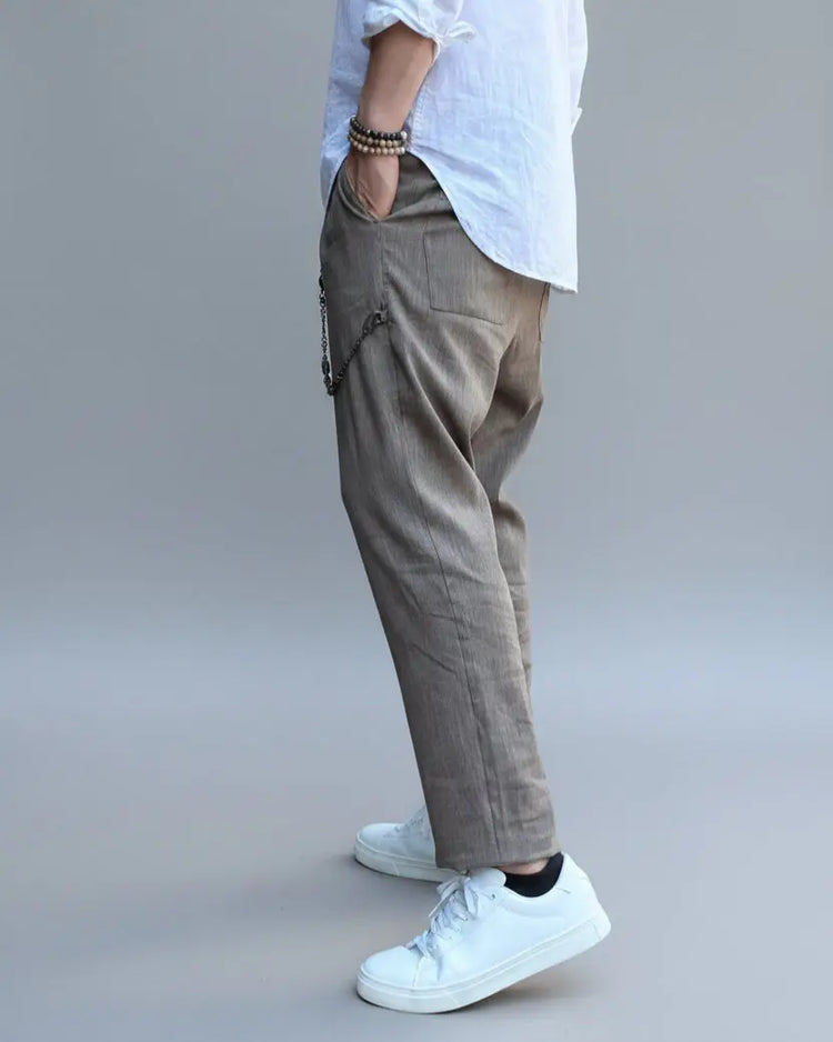 Model standing in front of light grey backdrop wearing brown linen pants and white shirt and sneakers