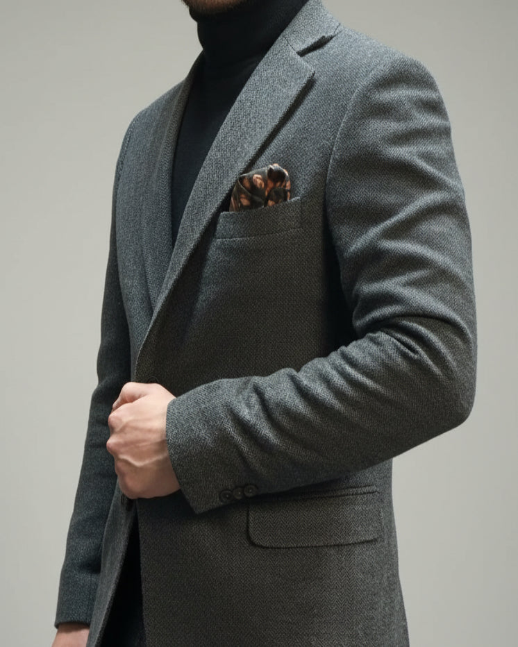 Grey herringbone suit jacket with a pocket square against a neutral background