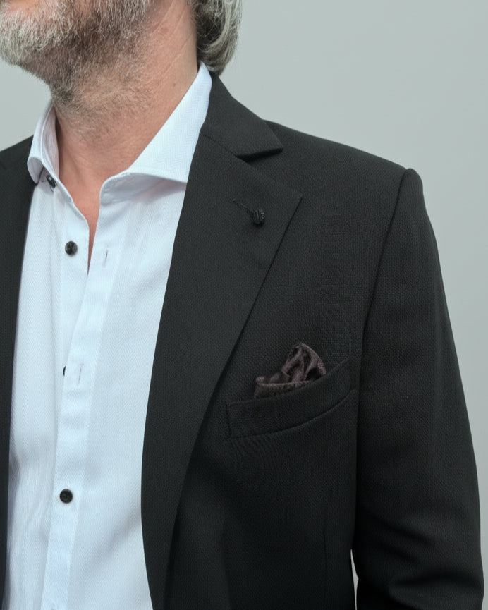 Model standing in front of light grey backdrop wearing black suit and white shirt.