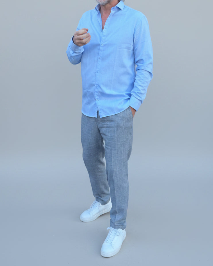 Man in light blue shirt and gray pants standing in front of light grey backdrop