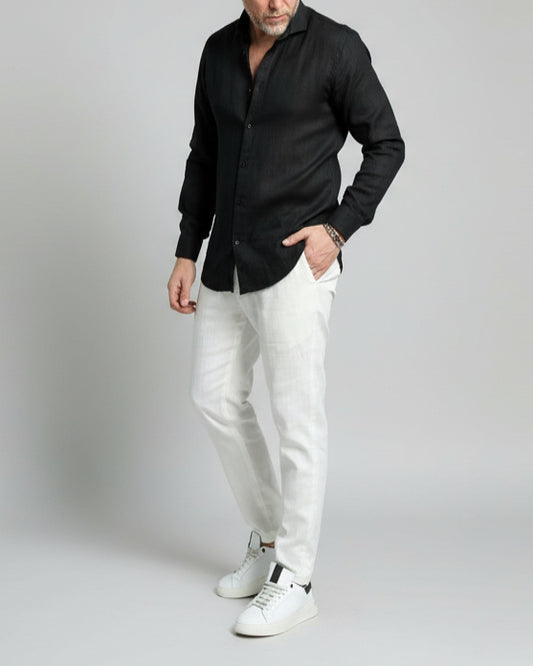 Model wearing a black linen shirt and white pants on a plain background