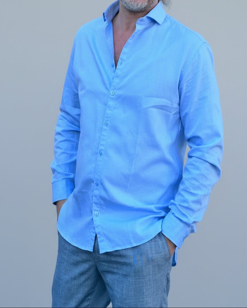 Man in light blue shirt and gray pants standing in front of light grey backdrop
