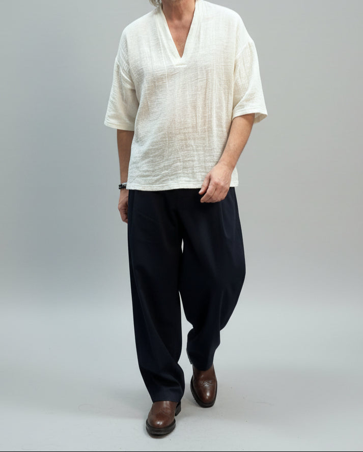 Person wearing a white shirt and dark pants standing on a pink platform with a neutral background.