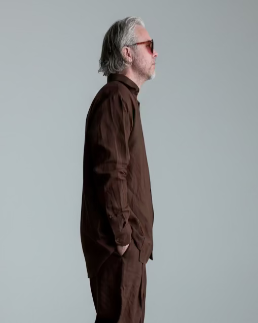 Man in a brown outfit standing against light grey backdrop