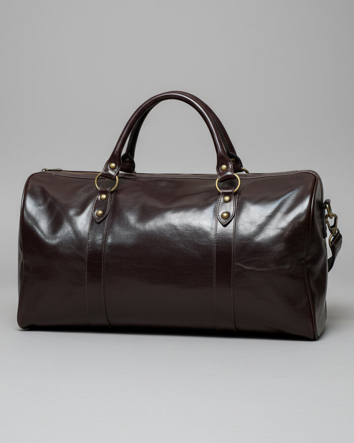 Brown leather duffel bag with a shoulder strap and 1 puller on the side pocket on a textured light grey surface