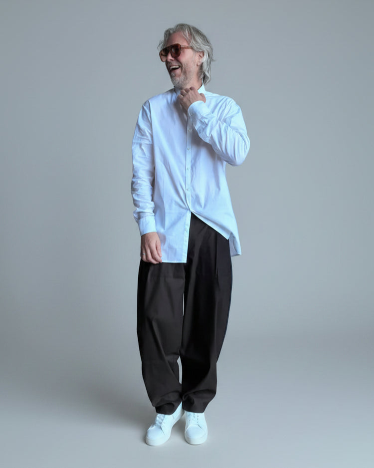 Person wearing a white shirt and dark pants standing against a light grey backdrop. keep position as it is