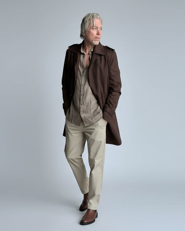 MODEL STANDING IN FRONT OF L. GREY BACKDROP WEARING A BROWN TRENCH COAT
