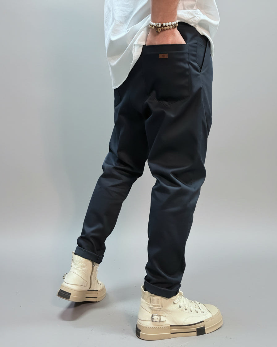 Person wearing blue pants and beige high-top sneakers in an industrial setting showing the back pocket with label on