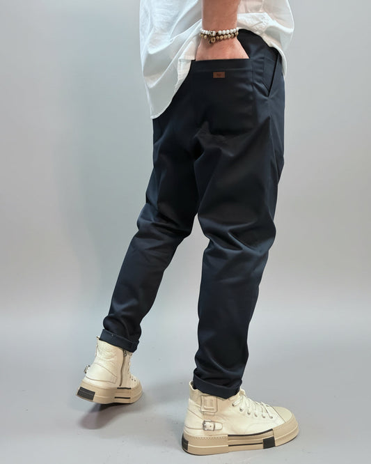 Person wearing blue pants and beige high-top sneakers in an industrial setting showing the back pocket with label on