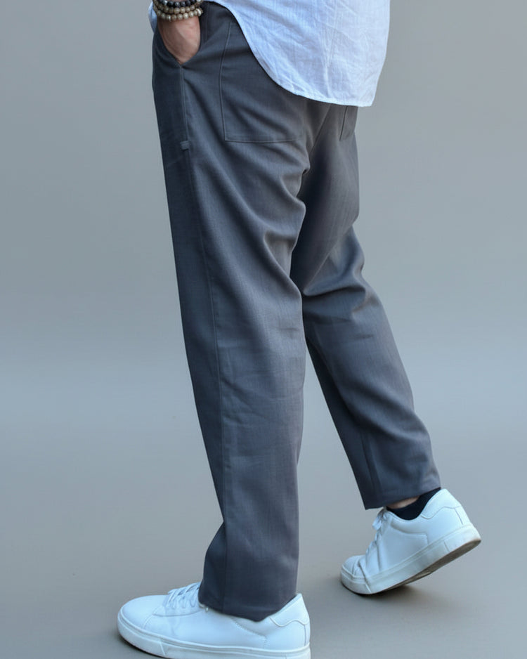 Person wearing a white shirt, grey linen pants, and white sneakers on a light grey background in a dynamic possition.