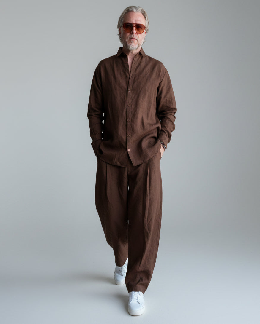 Man in a brown outfit standing against light grey backdrop