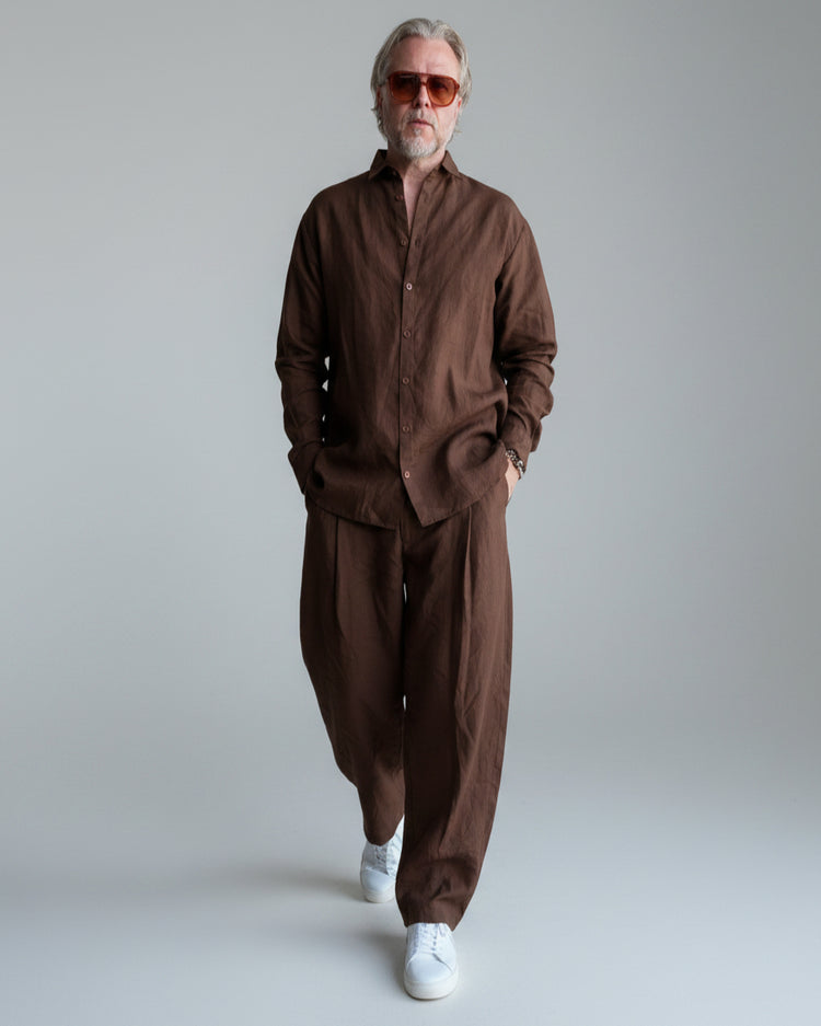Man in a brown outfit standing against light grey backdrop