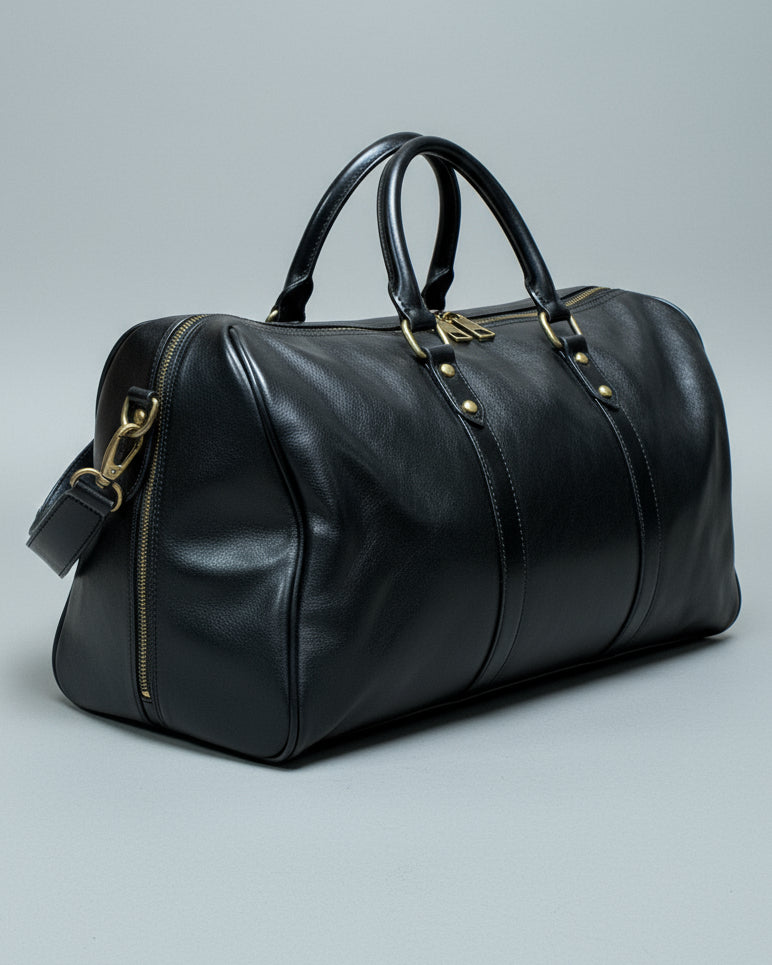 Black leather duffel bag with a shoulder strap and 1 puller on the side pocket on a textured light grey surface