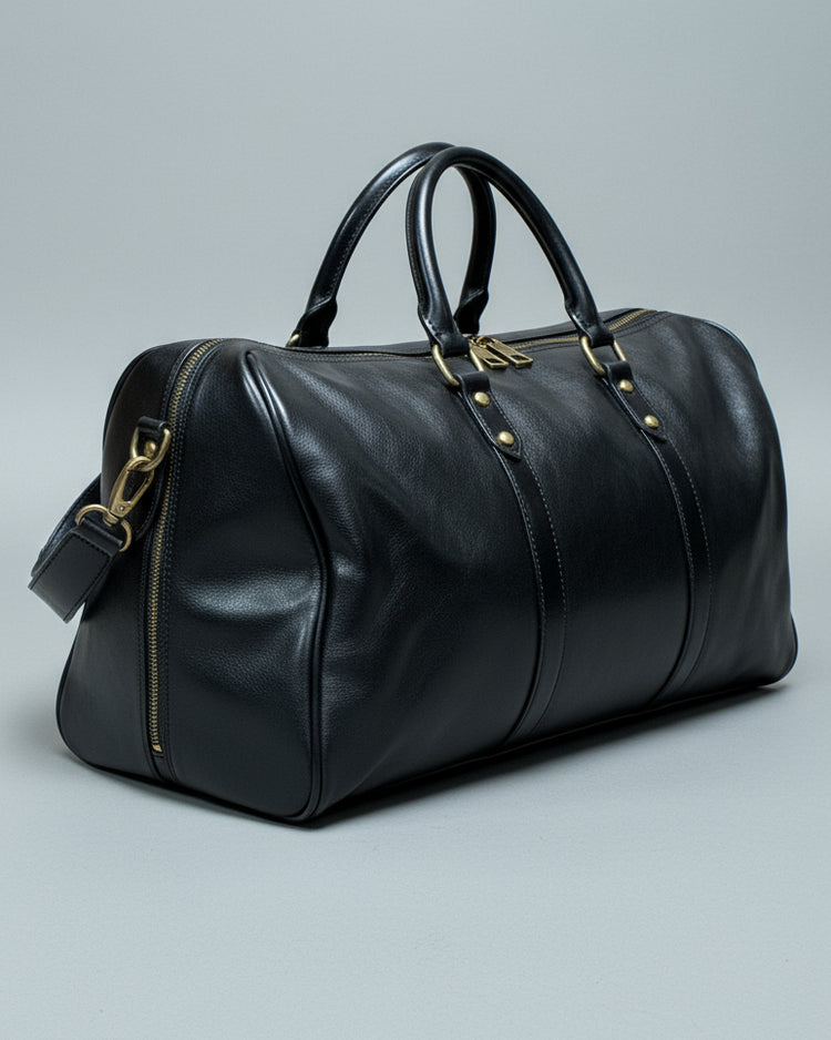 Black leather duffel bag with a shoulder strap and 1 puller on the side pocket on a textured light grey surface
