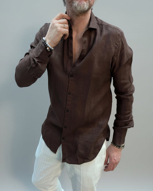 Model wearing a brown button-up shirt and white pants against light grey backdrop