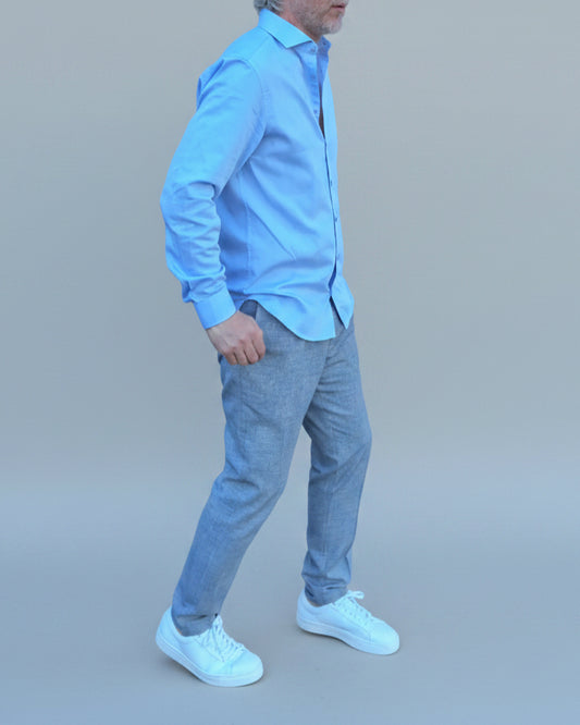 Man in light blue shirt and gray pants standing in front of light grey backdrop