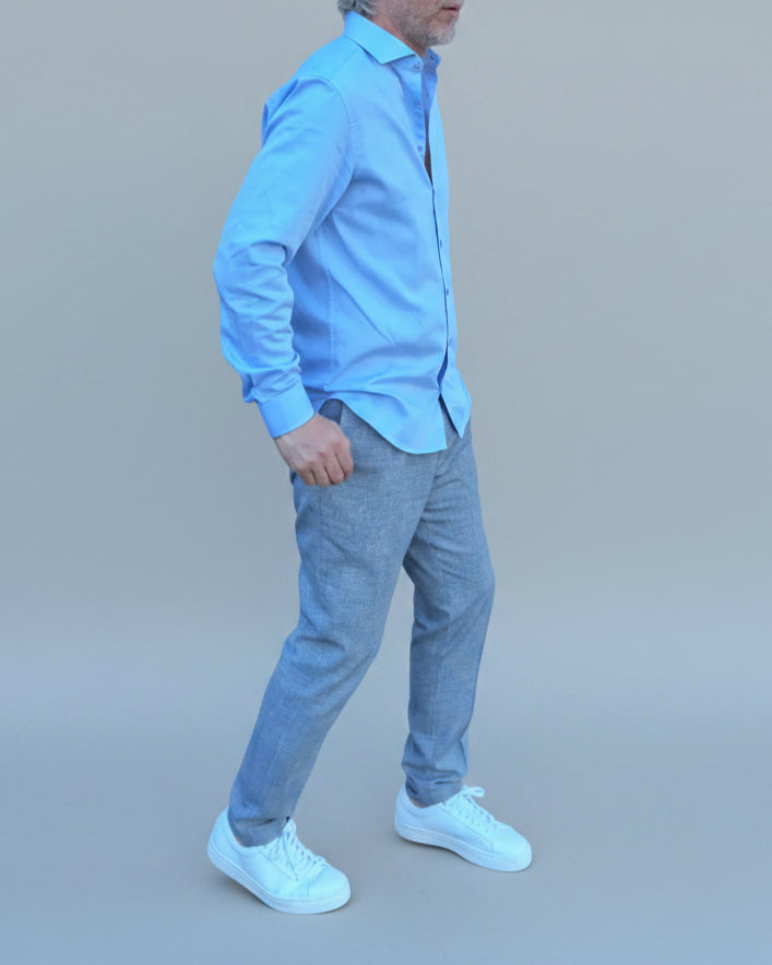 Man in light blue shirt and gray pants standing in front of light grey backdrop