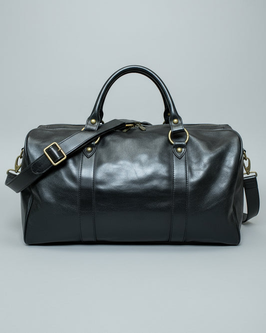 Black leather duffel bag with a shoulder strap and 1 puller on the side pocket on a textured light grey surface