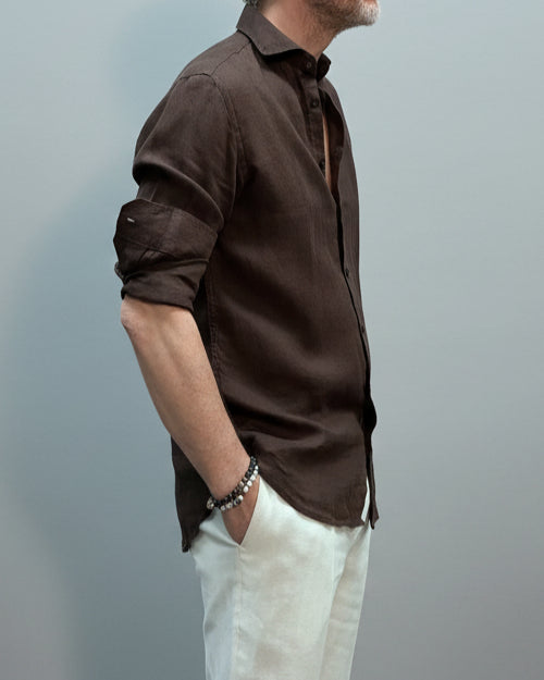 Model wearing a brown button-up shirt and white pants against light grey backdrop