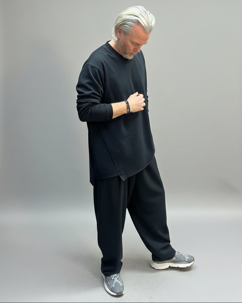 Man wearing a black outfit standing in front of beige backdrop 