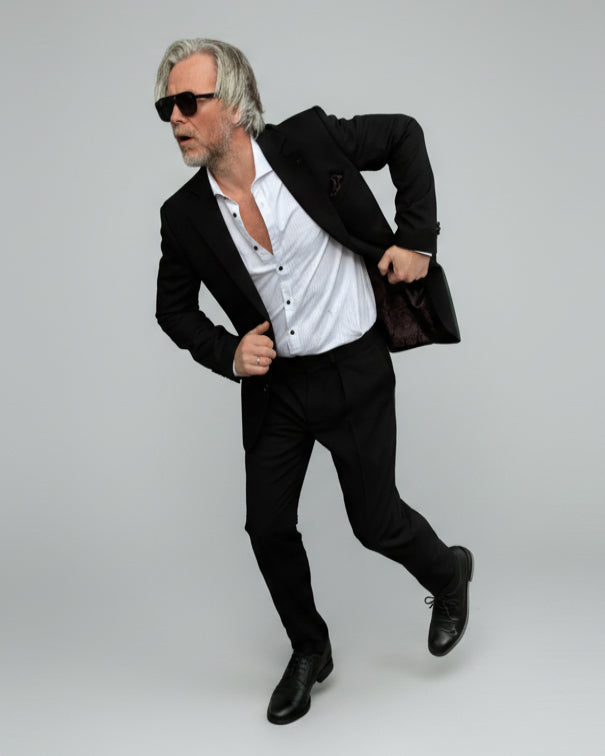 Model standing in front of light grey backdrop wearing black suit and white shirt.
