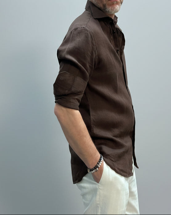 Model wearing a brown button-up shirt and white pants against light grey backdrop