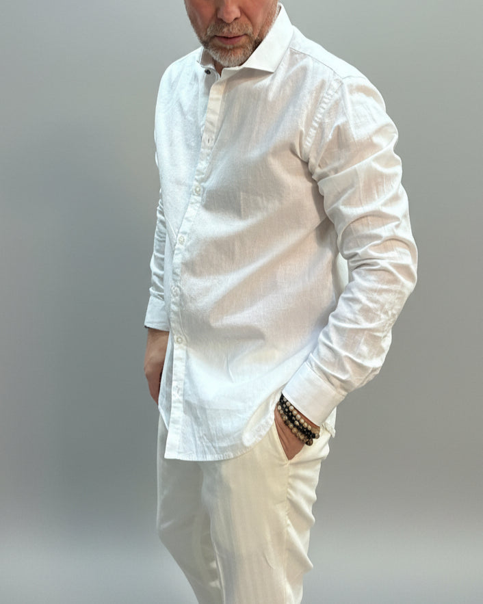 Model wearing a white linen shirt and pants in front of light grey backdrop 