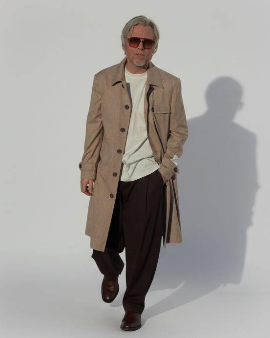 MODEL WEARING A BEIGE COAT IN FRONT OF A GREY BACKDROP