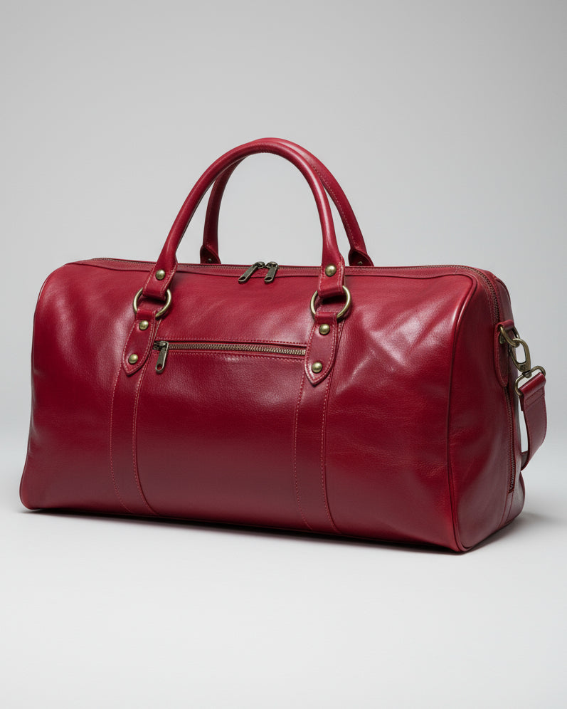 Red leather duffel bag with shoulder strap and 1 puller on outside pocket on a light gray background