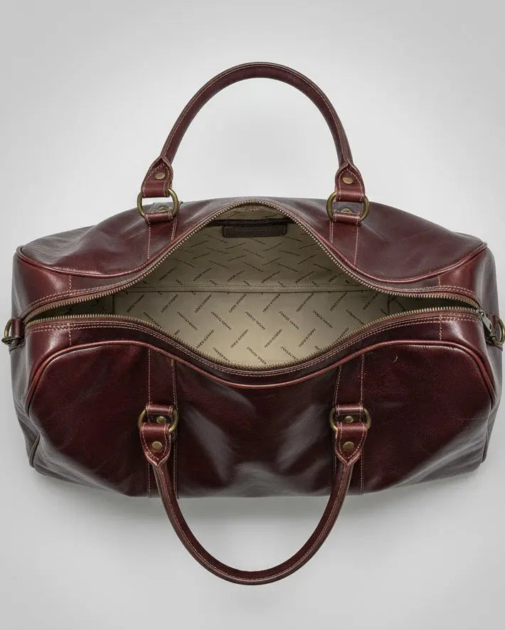 Brown leather bag with gold hardware and shoulder strap and one puller on zipper in front pocket on a light gray background