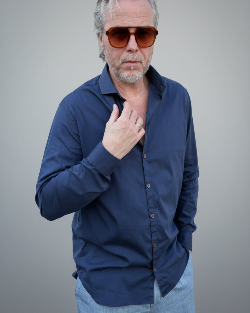 Person wearing a navy blue button-up shirt in front of light grey backdop