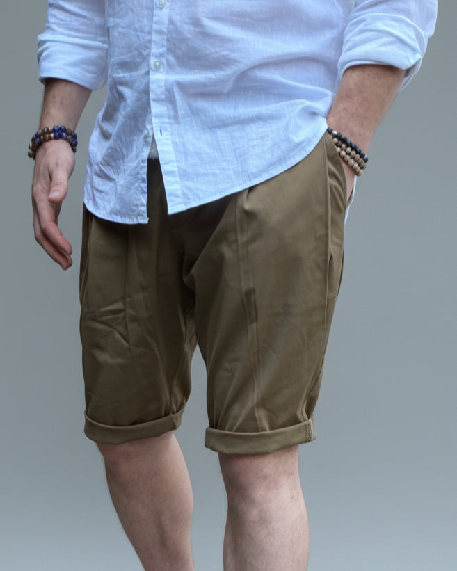 Person wearing a white shirt, brown shorts, and white sneakers in front of light grey backdrop.