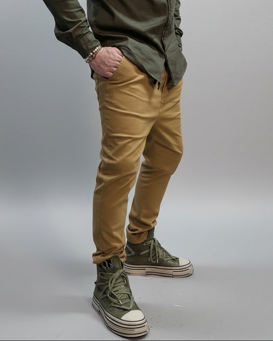Person wearing a green shirt, beige pants, and green high-top sneakers in a room with black walls and concrete floor. in a dynamic position 