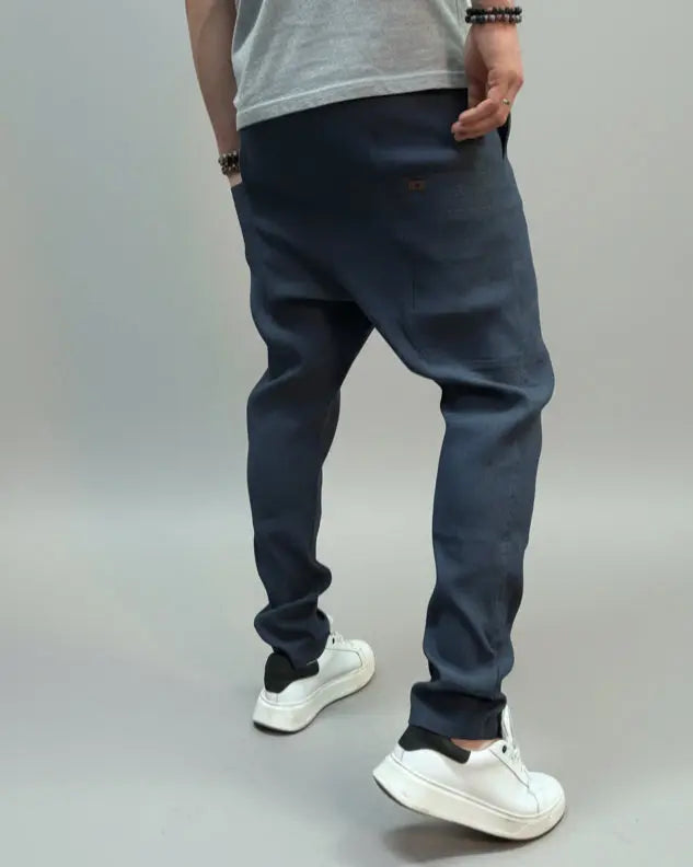 Person wearing a white T-shirt and blue pants standing on a gray floor with a brown fabric draped over them.
