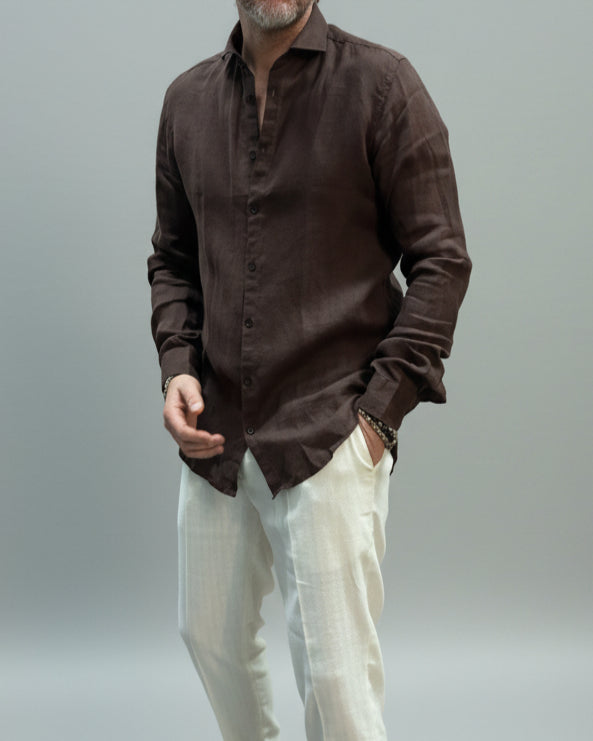 Model wearing a brown button-up shirt and white pants against light grey backdrop