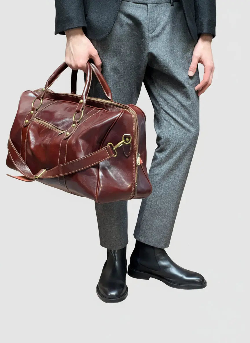 Person holding a brown leather backpack with shoulder strap  and one  puller on front pocket on  a beige surface