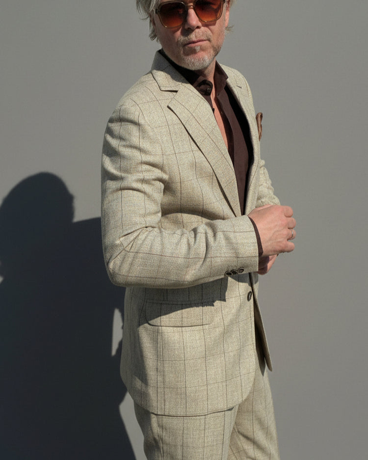 Model in a beige checked suit standing against a light grey backdrop