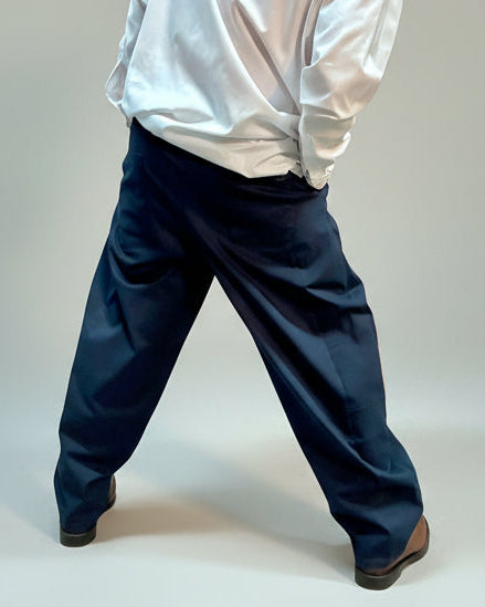 Person wearing a white shirt and blue pants standing backwards in front of light grey backdrop.