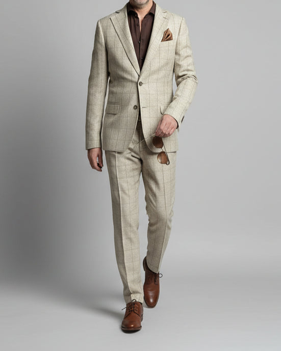 Man in a light-colored suit standing against a wall with a reflective surface.