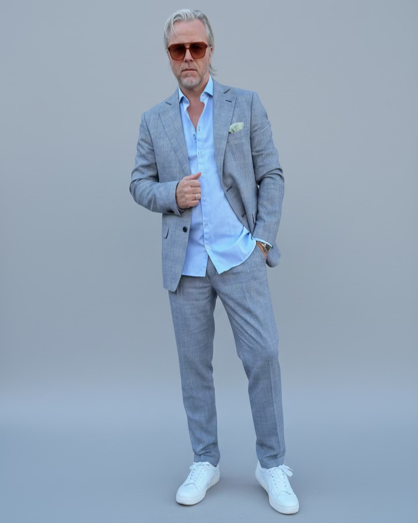 Man in a gray, blue checked suit standing in front of a light grey backdrop.