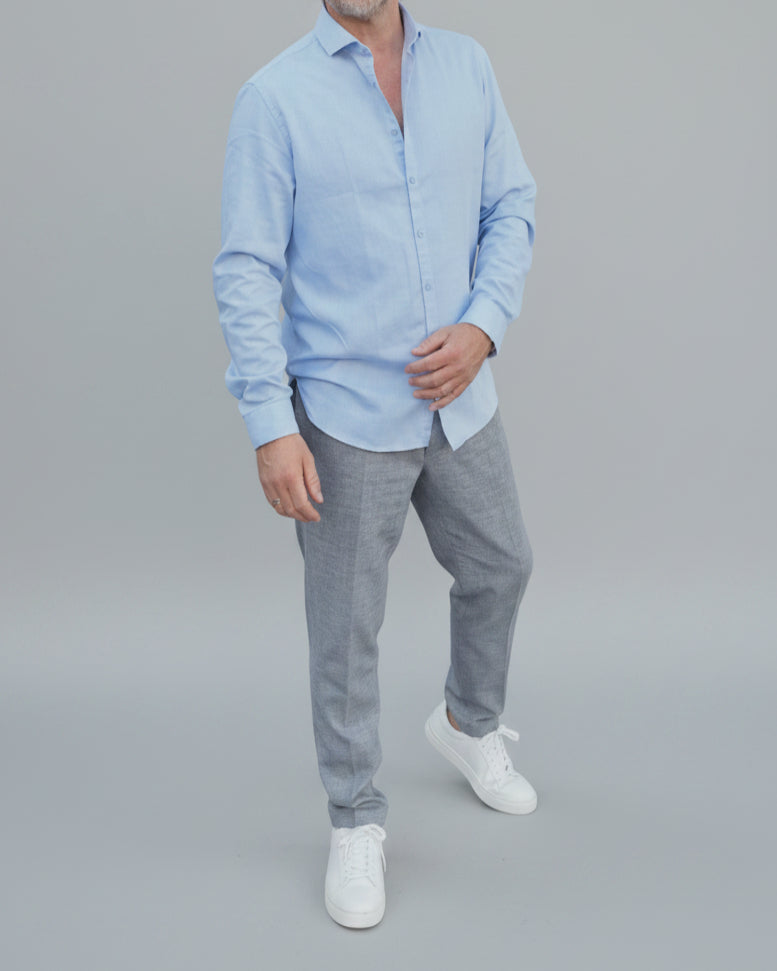 Man in light blue shirt and gray pants standing in front of light grey backdrop